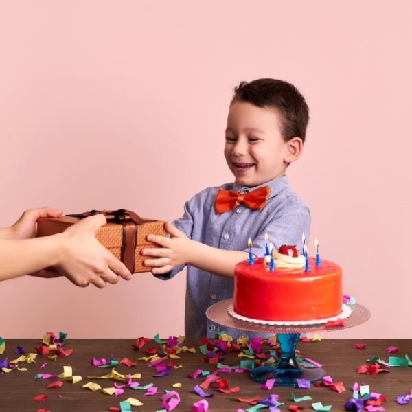 Geburtstagsfreude für kleine Helden Lachender Junge mit roter Geburtstagstorte erhält ein Geschenk – fröhlicher Moment voller Überraschung und Konfetti